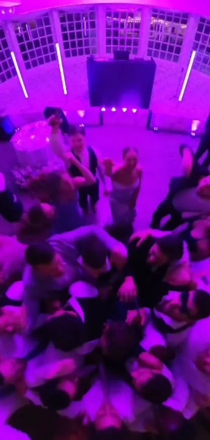 A crowd dancing with hands raised under purple lights