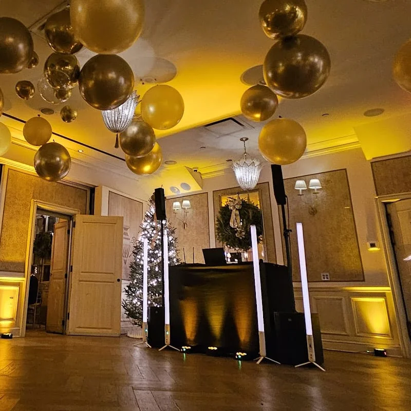 DJ booth and lighting set up in a ballroom decorated with gold and black balloons
