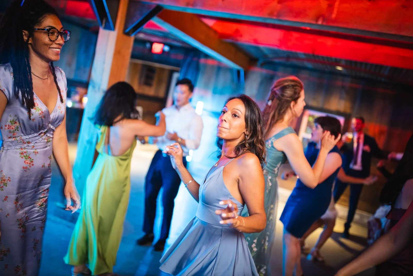 Guests in formal dresses dancing under red lighting in a barn venue