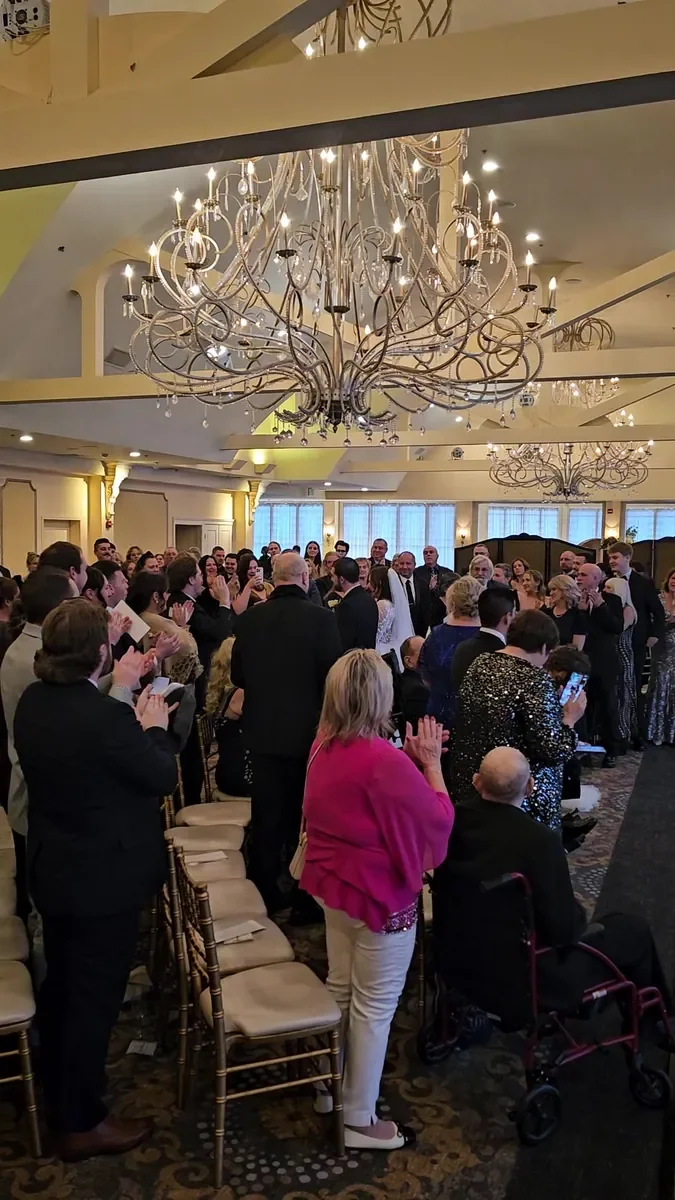 Guests standing in a ballroom with large chandeliers during a wedding ceremony