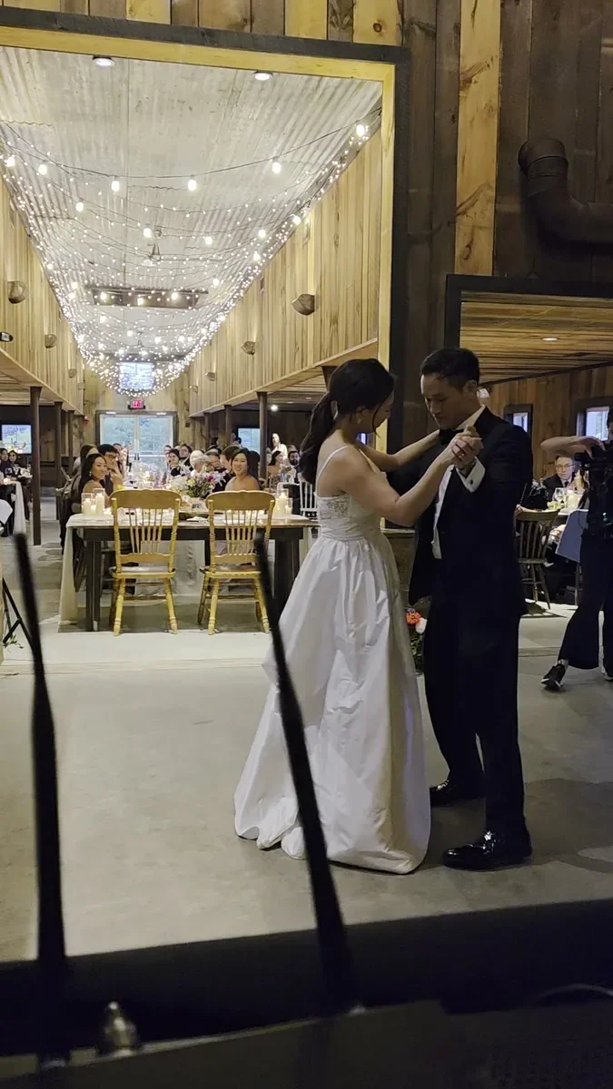 A bride and groom sharing their first dance under string lights in a barn venue