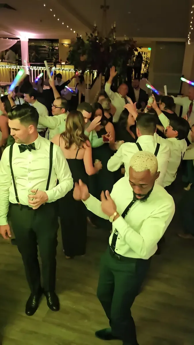 Wedding guests in suspenders and bow ties dancing with light-up sticks on a packed dance floor