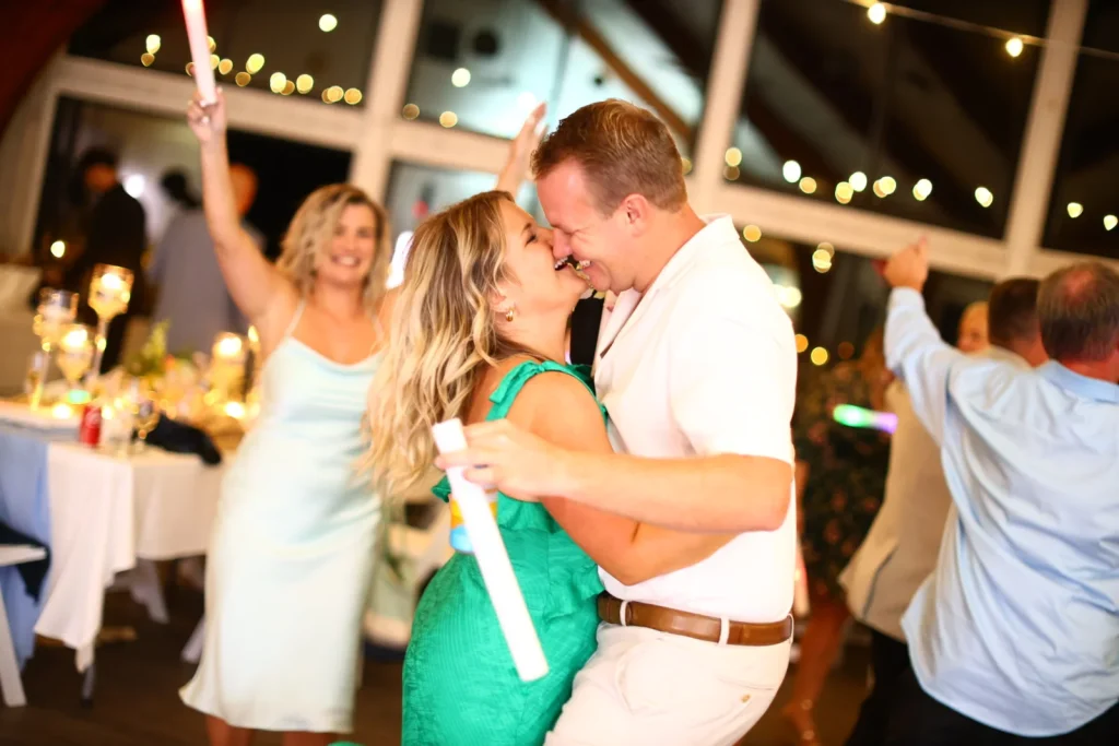 Wedding guests dancing and hugging with light-up foam sticks under string lights